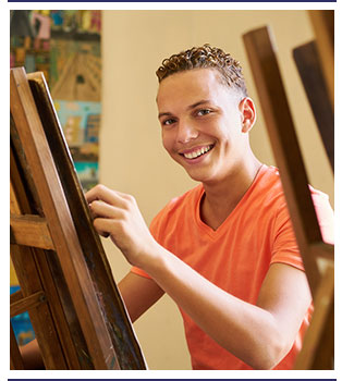Smiling student works on an art project using an easel