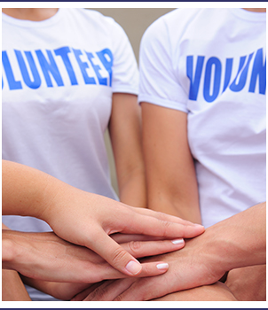 Students wearing volunteer shirts stack their hands on top of each other