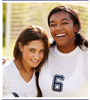 Two students wearing soccer attire pose in front of a soccer goal outside